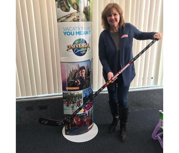 A woman holding a hockey stick in a room with grey carpeting 